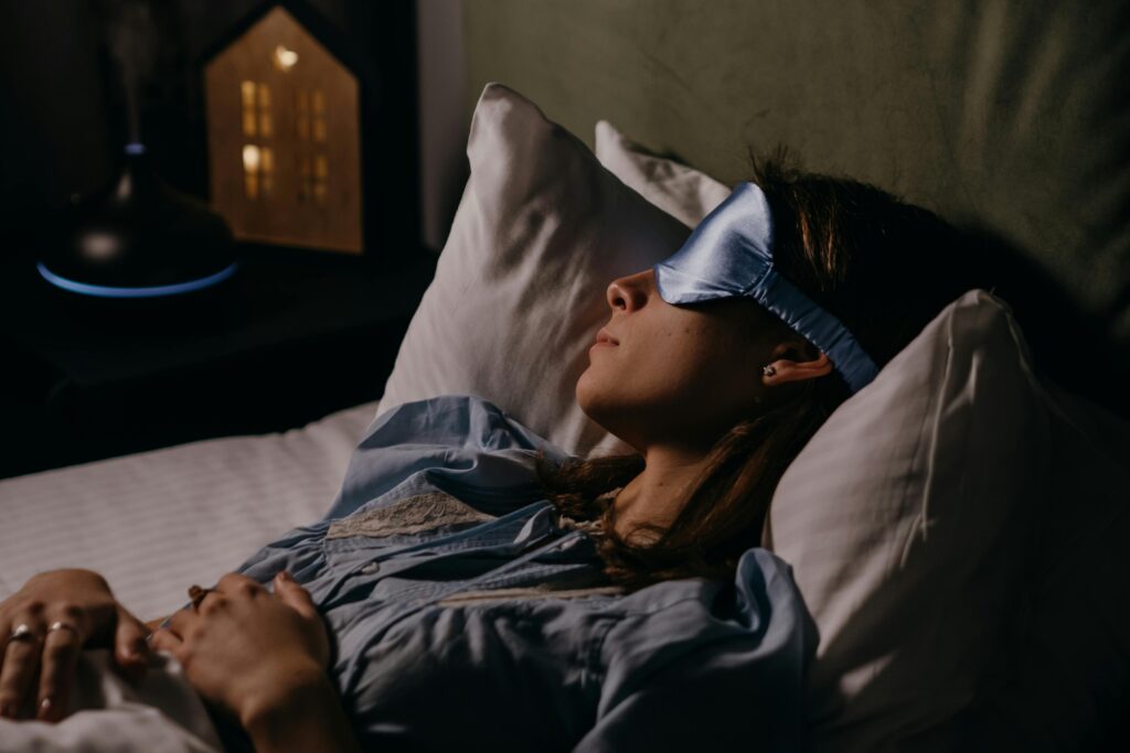 How screentime keeps your mind awake at night A woman sleeping peacefully wearing a blue eye mask in a cozy, dimly lit bedroom.