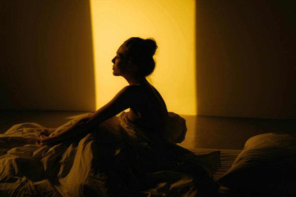 How screentime keeps your mind awake at night A silhouette of a woman sitting in bed with warm sunlight streaming in.